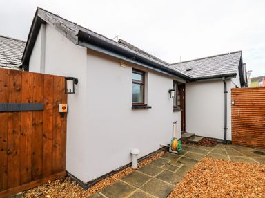 The exterior of a white building with two windows a brown door two wooden fences paving stones and gravel at Llygad Y Dydd in Bow Street Wales