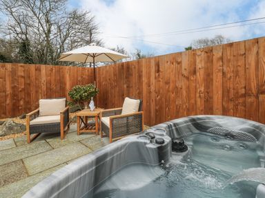 An outdoor patio area with two chairs a small table with glasses and bottle a patio umbrella and a hot tub at Llygad Y Dydd in Bow Street Wales