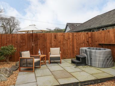A patio with chairs a small table an umbrella and a hot tub at Llygad Y Dydd in Bow Street Wales