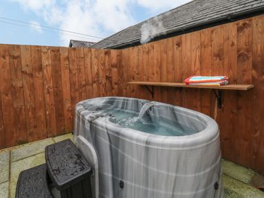 An outdoor hot tub with water flowing into it and a wooden fence with a shelf and towels at Llygad Y Dydd in Bow Street Wales