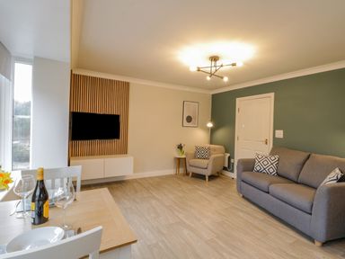 A living room with a gray sofa an armchair dining table with wine and glasses and a wall-mounted TV at Estuary Walk in Whitby