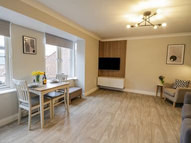 A living room with a dining table set near windows and a wall-mounted TV at Estuary Walk in Whitby