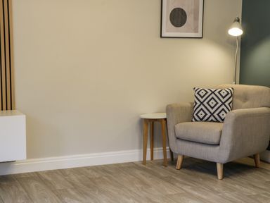 A beige armchair with a patterned cushion next to a small round table and a floor lamp in a room at Estuary Walk Whitby