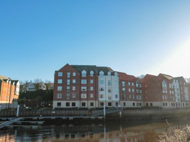 A row of brick and white residential buildings by a river with docks at Estuary Walk in Whitby