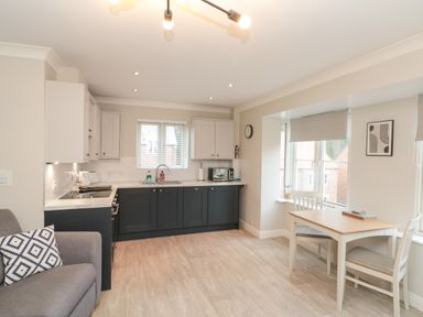 A kitchen with dark lower cabinets and light upper cabinets with a dining table and chairs by windows at Estuary Walk in Whitby