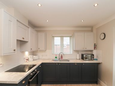 A kitchen with white upper cabinets black lower cabinets a stovetop oven toaster microwave and a clock on the wall at Estuary Walk in Whitby
