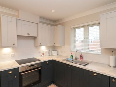A kitchen with dark lower cabinets white upper cabinets an oven a stove a sink under a window and kitchen appliances at Estuary Walk in Whitby