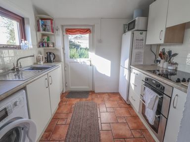 A kitchen with tiled floor a sink washing machine oven and refrigerator at Hillcrest in Oxwich near Port Eynon