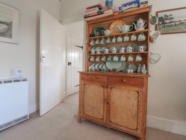 A wooden kitchen cabinet with cups plates and board games on top in a room at Hillcrest in Oxwich near Port Eynon