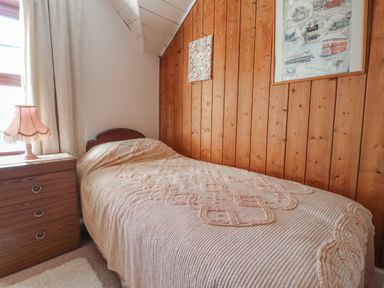 A small bedroom with a single bed and a bedside table with a lamp and wooden panel wall in Hillcrest Oxwich near Port Eynon
