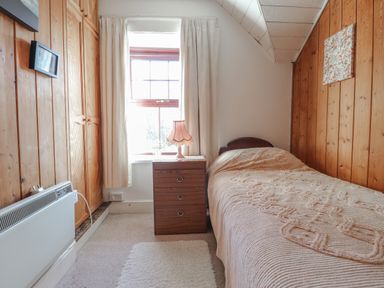 A small bedroom with a single bed wooden panel walls a wooden nightstand and a window with curtains at Hillcrest in Oxwich near Port Eynon