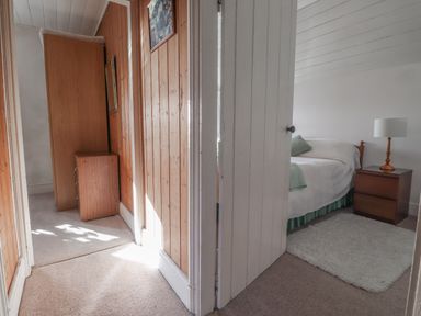 A hallway with wooden paneling and a small cabinet leading to a bedroom with a bed a bedside table and a lamp at Hillcrest in Oxwich near Port Eynon