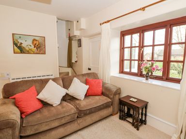 A living room with a brown sofa and cushions next to a window with a vase of flowers on the sill at Hillcrest Oxwich near Port Eynon