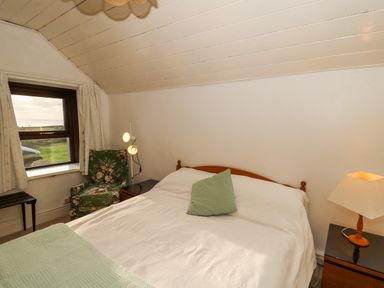 A bedroom with a bed a green pillow a green armchair a window and two bedside tables with lamps at Hillcrest Oxwich near Port Eynon