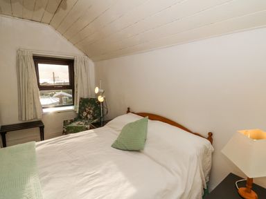A bedroom with a bed a green pillow a window with curtains a floral armchair two lamps and a small table at Hillcrest in Oxwich near Port Eynon