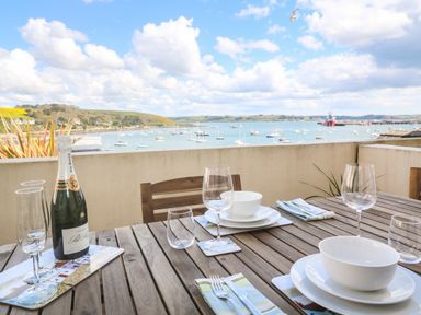A wooden outdoor dining table set with glassware, plates, bowls, and a bottle of champagne overlooking a harbor with boats at 58 High Street in Falmouth
