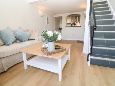 A living room with a beige sofa and blue cushions a wooden coffee table with a flower vase and a staircase with dark tiles at 58 High Street Falmouth