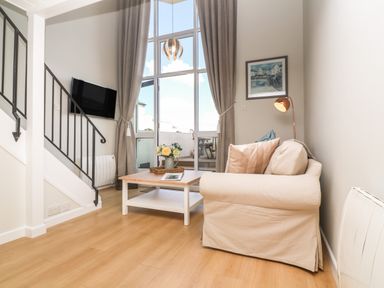 A living room with a beige sofa a wooden coffee table a wall-mounted television and a staircase at 58 High Street in Falmouth