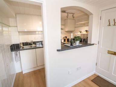 A kitchen with white cabinets a sink a washing machine a bottle of champagne and a flower pot on the counter at 58 High Street in Falmouth