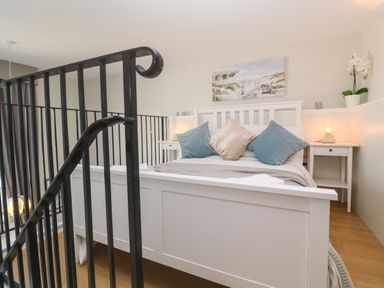 A bedroom with a white bed, blue and beige pillows, nightstands with lamps, a painting on the wall and black metal railings at 58 High Street in Falmouth
