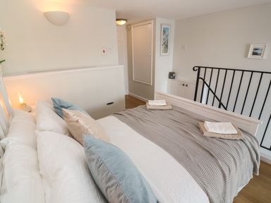 A bedroom with a bed made with pillows and folded towels near a staircase with black railing at 58 High Street in Falmouth