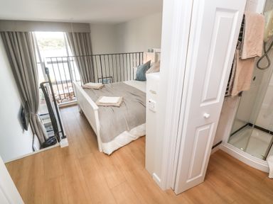 A bedroom with a double bed next to a railing and a bathroom with a shower behind a door at 58 High Street in Falmouth