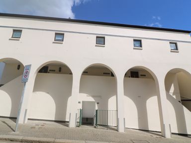 A white building with arched doorways and small windows under a blue sky at 58 High Street in Falmouth