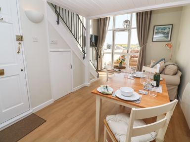 A dining area with a wooden table set for four people next to a small living area with a sofa and a door leading to an outdoor patio at 58 High Street in Falmouth
