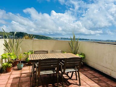 An outdoor terrace with wooden table and chairs and potted plants with a view of hills and sky at 58 High Street in Falmouth