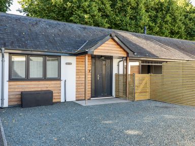 An entrance of a single story house with wooden paneling a black door and gravel driveway at Clonmore in Bodmin