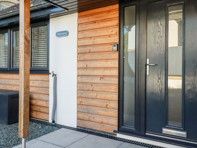 A front door with glass panels beside wooden paneling and a white wall with a water tap at Clonmore in Bodmin