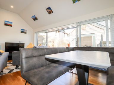 A living area with a corner bench and table near large windows and a seating area with a television and cushions at Clonmore in Bodmin