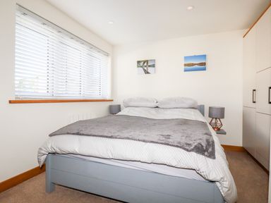A bedroom with a bed with gray and white bedding two bedside tables with lamps and wardrobe in Clonmore Bodmin