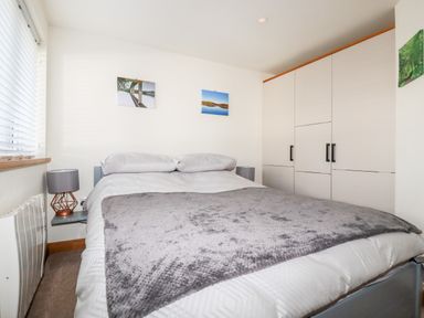 A bedroom with a bed covered in white bedding and a gray blanket with a wardrobe and bedside lamps at Clonmore in Bodmin