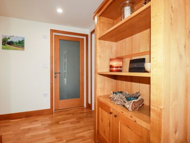 A wooden cabinet with shelves and decorations next to a wooden door with frosted glass in a hallway at Clonmore in Bodmin