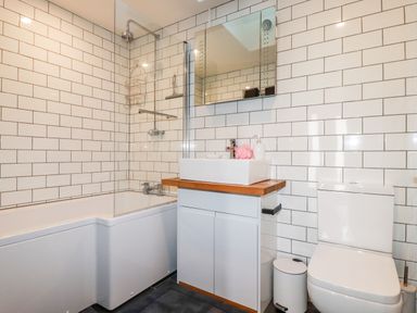 A bathroom with a bathtub shower combination a sink with wooden countertop a mirror a toilet and white tiled walls at Clonmore in Bodmin