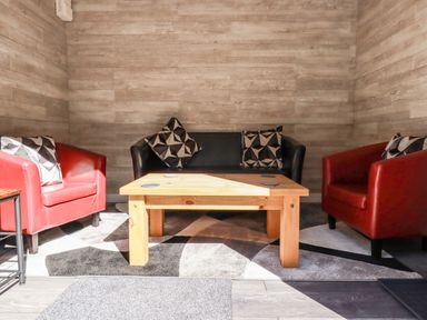A seating area with a black sofa and two red armchairs around a wooden coffee table at Clonmore in Bodmin