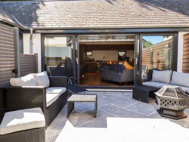 An outdoor patio area with black wicker furniture and cushions facing glass sliding doors at Clonmore in Bodmin