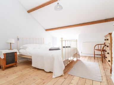 A bedroom with a white metal bed frame wooden floor wooden furniture and ceiling beams at Trelash Cottage in Trelash near Boscastle