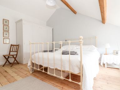 A bedroom with a metal frame bed wooden chair white wardrobe and bedside table with lamp at Trelash Cottage Trelash near Boscastle