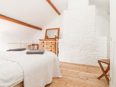 A bedroom with a white bed, wooden dresser with mirror, wooden chair, and wooden floor at Trelash Cottage in Trelash near Boscastle