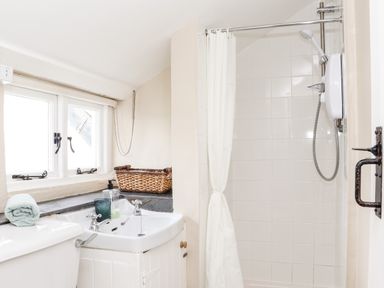 A bathroom with a white sink, wicker basket, and shower with curtain at Trelash Cottage in Trelash near Boscastle
