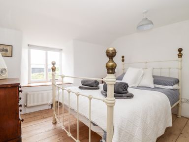 A bedroom with a white metal bed frame wooden chest of drawers and a window at Trelash Cottage in Trelash near Boscastle
