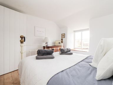 A bedroom with a double bed with folded towels on it a wooden chest of drawers a table lamp and a window at Trelash Cottage Trelash near Boscastle