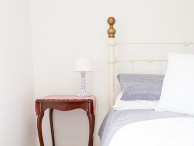A bedside table with a lamp next to a bed with pillows and checked bedding at Trelash Cottage in Trelash near Boscastle