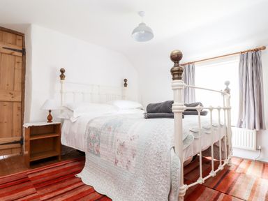 A bedroom with a white metal bed frame bedside table with lamp striped curtains and a striped carpet at Trelash Cottage in Trelash near Boscastle