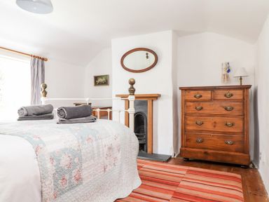 A bedroom with a bed a wooden chest of drawers a fireplace and a striped rug at Trelash Cottage Trelash near Boscastle