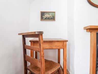 A small wooden table and chair against a white wall with a painting of flowers hanging above at Trelash Cottage in Trelash near Boscastle