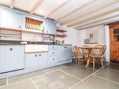 A kitchen with blue cabinets a farmhouse sink wooden dining table with chairs and wooden ceiling beams at Trelash Cottage Trelash near Boscastle