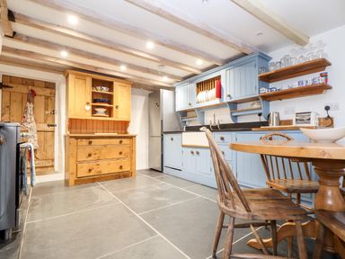 A kitchen with blue cabinets wooden chairs a wooden table and a wooden cupboard at Trelash Cottage in Trelash near Boscastle